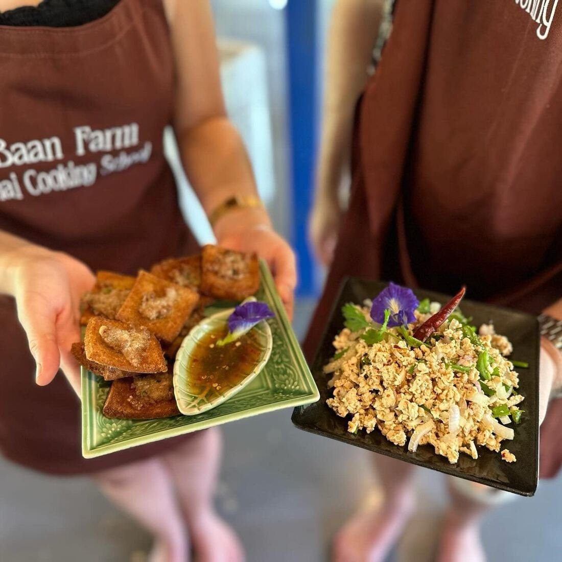 Guests holding plates of spring rolls and salad wearing Baan Farm Thai Cooking School aprons